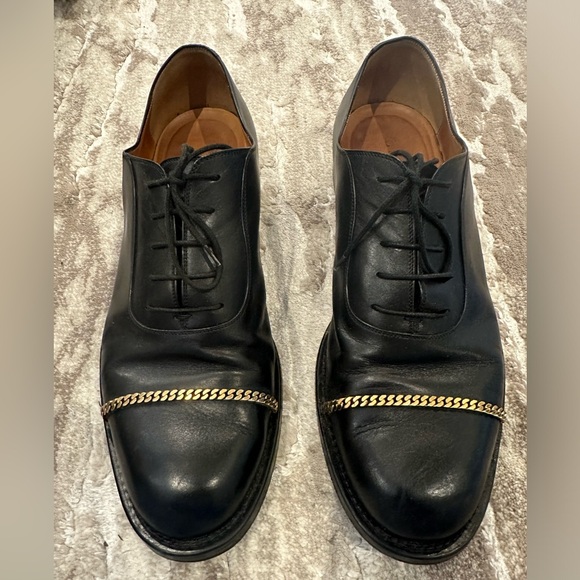 Gucci men’s black dress shoe with gold chain hardware.